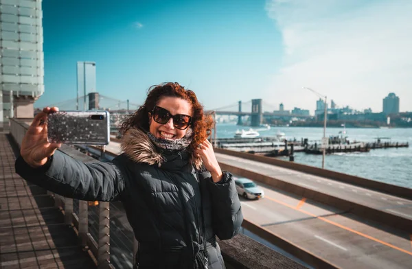 Güzel kıvırcık esmer kadın New York arka planında Brookling köprüsü ile kendi portresini çekiyor. — Stok fotoğraf