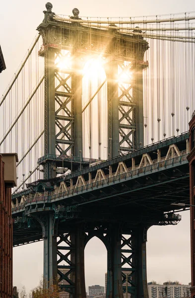 El sol viaja a través de un pilar del puente Manhattan visto desde el distrito Dumbo en Brooklyn — Foto de Stock