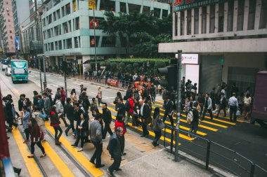 Bir tramvay istasyonunun önünde karşıdan karşıya geçen bir kalabalık..
