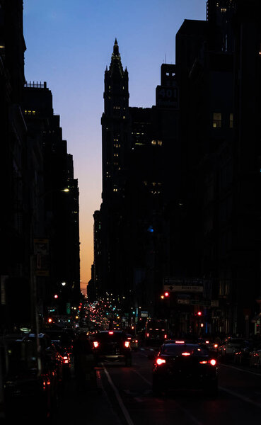 Sunset view of Broadway street from Soho with the financial skyline and the Woolworth building silhouette on the background, New York.