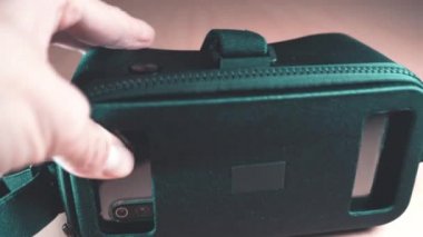 Erkek eli VR gözlüklü birinin içindeki akıllı telefonu çıkarıyor.