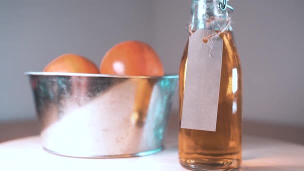Nahaufnahme von Glasflasche mit Apfelsaft und Äpfeln im Korb auf Holztischplatte — Stockvideo