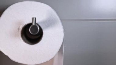 Macro view of a roll of white toilet paper in a tiled bathroom