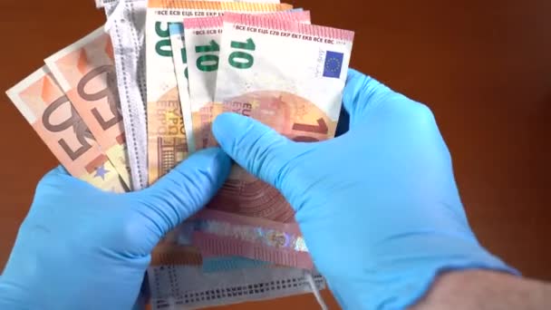 Hand med blå medicinska handskar, Euro räkningar och en ansiktsmask med ordet coronavirus — Stockvideo