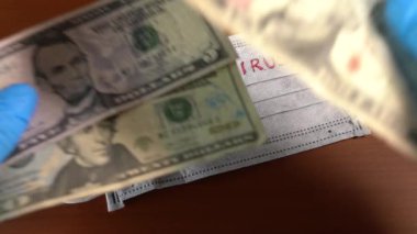 Yüz maskesini koronavirüsle kaplayan dolarlarla dolu bir el.