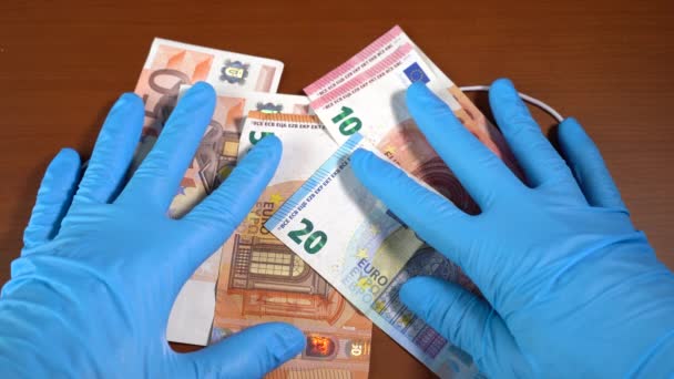 Hand with euro bills uncovering a face mask with the word coronavirus — Stock Video