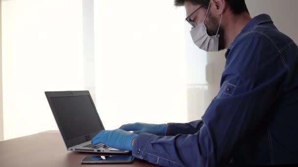 Hombre con mascarilla facial y guantes azules trabajando desde casa y preocupado por el coronavirus covid-19 — Vídeo de stock