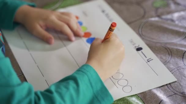 Close-up view of a child drawing with crayons on paper or doing homework from home — Stock Video