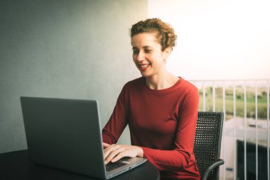 Karantina sırasında uzaktan eğitim. Balkonda dizüstü bilgisayarda çalışan bir kadın. Serbest İşçi, uzak çalışma.