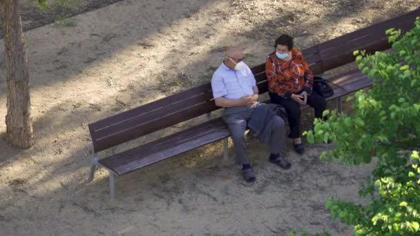 Reus, España. Mayo 2020: Pareja mayor con máscaras fasce sentada en un banco del parque . — Vídeos de Stock