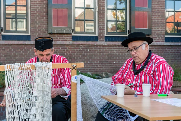 Dutch fair with men in traditional clothing repairing fishing nets — Stock Photo, Image