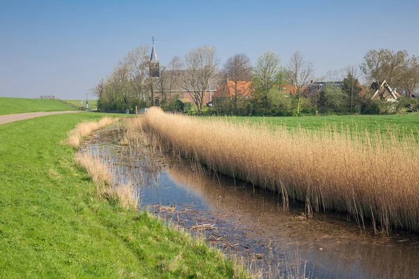 Aldeia holandesa Gaast com igreja atrás da barragem para proteção do mar — Fotografia de Stock