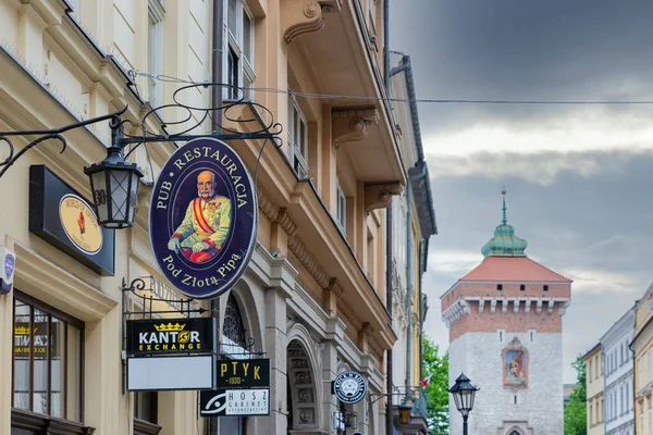 Skyltar i Krakow maiin shoppinggata med Florianska Brama torn — Stockfoto