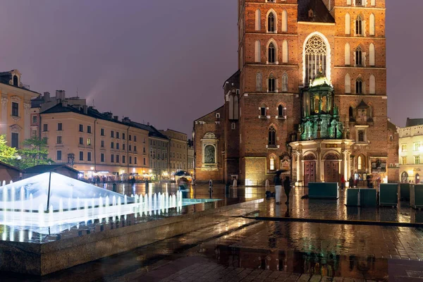 Plaza del mercado nocturno lluvioso Cracovia con iglesia y fuente, Polonia — Foto de Stock