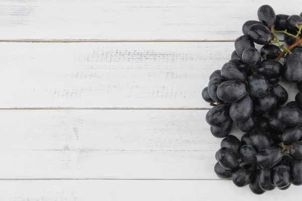 Frische schwarze Trauben mit Wassertropfen auf weißem Holz — Stockfoto