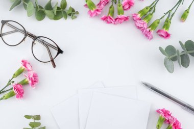Boş beyaz kart, gözlük ve kalem pembe karanfil çiçeklerle dekore edilmiş ve kopya alanı ile beyaz arka plan üzerinde bebek okaliptüs yaprakları