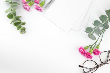 Boş beyaz kart, gözlük ve kalem pembe karanfil çiçeklerle dekore edilmiş ve kopya alanı ile beyaz arka plan üzerinde bebek okaliptüs yaprakları