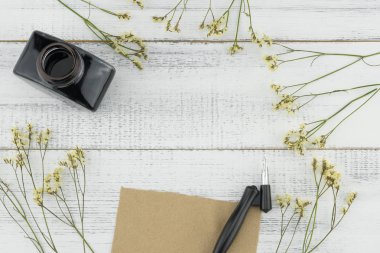 Boş kahverengi kart, eğik kalem ve mürekkep şişe beyaz ahşap zemin üzerine sarı limonium caspia çiçeklerle dekore edilmiş 