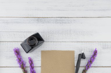 Boş kahverengi kart, eğik kalem ve mürekkep şişesi ile Menekşe liatris çiçekleri beyaz tahta arka plan kopya alanı ile dekore edilmiş