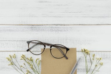 Boş kahverengi kart, kalem ve kopya alanı Beyaz ahşap zemin üzerine sarı limonium caspia çiçeklerle süslenmiş gözlük