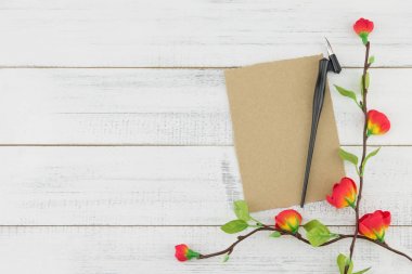 Beyaz ahşap arka plan kopya alanı ile sahte kırmızı çiçek dallarda boş kahverengi kart ve eğik kalem süslenmiş