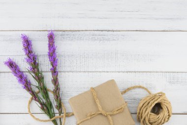 Kahverengi hediye kutusu ve ip kopya alanı Beyaz ahşap zemin üzerine Menekşe liatris çiçeklerle dekore edilmiş