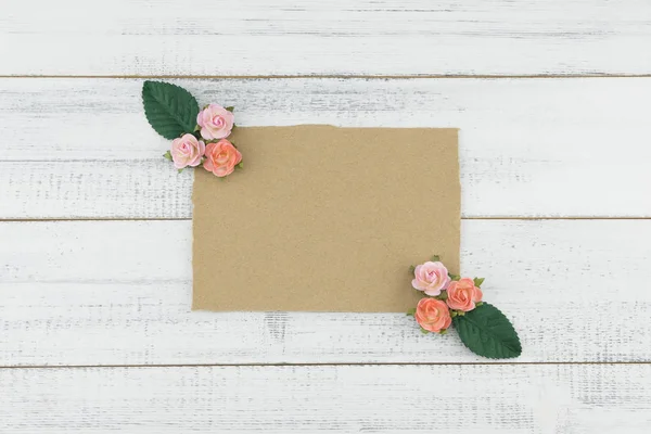 Blank brown card decorate with pink rose paper flowers and green leaves on white wood background