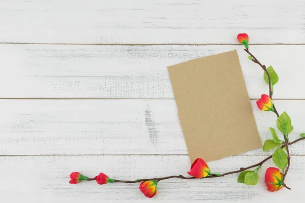 Blank brown card decorated with fake red flowers branches on white wood background with copy space