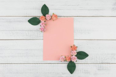 Boş pembe kart pembe Gül kağıt çiçeklerle süslemek ve Beyaz ahşap zemin üzerine yeşil yaprakları
