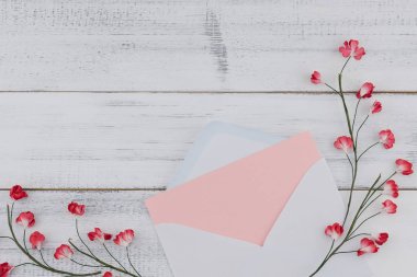 Beyaz zarf içinde boş pembe kart süslemek kopya alanı beyaz ahşap zemin üzerine kırmızı kağıt çiçeklerle