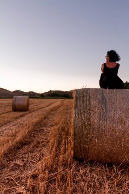 Beyaz, 30 'lu yaşlarda esmer bir kadın. Altın saat boyunca saman balyasının üzerinde oturuyor.
