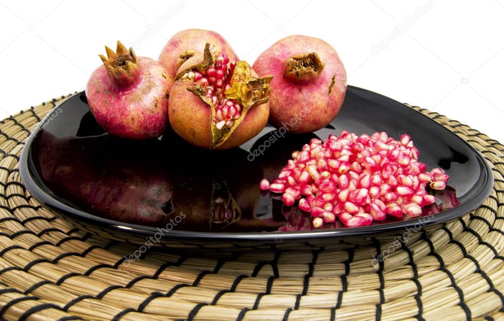 Group of pomegranades fruits and fresh seeds on a black dish and wooden plate. for food and healthy concepts