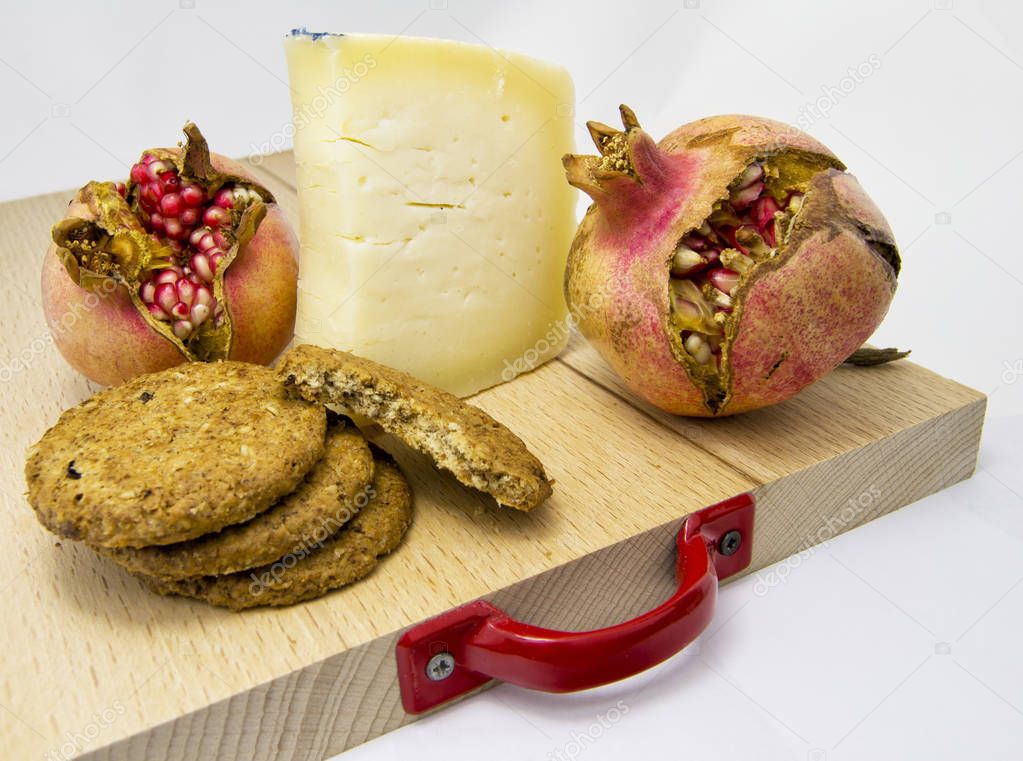 wood chopping board with assortment of cheeses, cookies and pomegranate fruit. for food concept