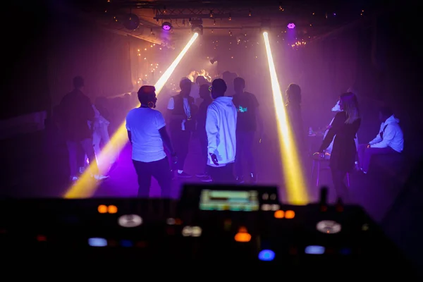 People dance on the dance floor at a techno night club party. View from the DJ console.