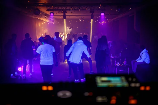 People dance on the dance floor at a techno night club party. View from the DJ console.