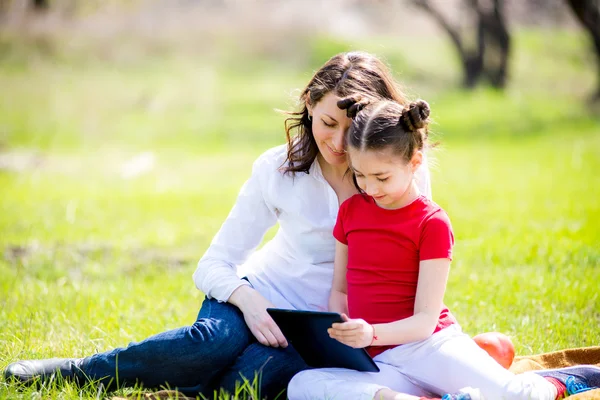 Madre e hija usando tableta digital mientras están sentadas en la hermosa naturaleza , —  Fotos de Stock