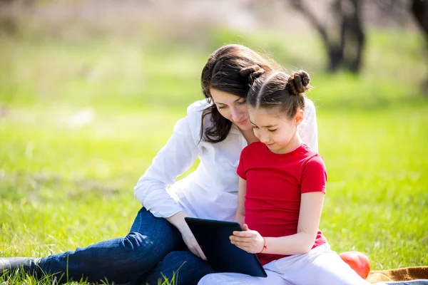 Madre e hija usando tableta digital mientras están sentadas en la hermosa naturaleza , —  Fotos de Stock