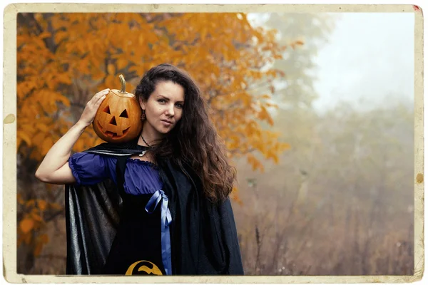 Jonge vrouw in Halloween kostuum in de herfst bos met gele pompoen witch. — Stockfoto