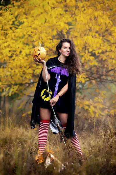 Jeune femme en costume de sorcière Halloween dans la forêt d'automne avec citrouille jaune . — Photo