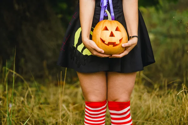 Fancy woman on Halloween in the forest, holding in hands pumpkin with carved face — Stock Photo, Image