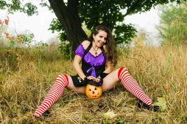 Jonge vrouw in Halloween kostuum in de herfst bos met gele pompoen witch. — Stockfoto