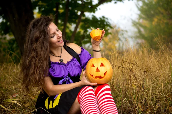 Jeune femme en costume de sorcière Halloween dans la forêt d'automne avec citrouille jaune . — Photo