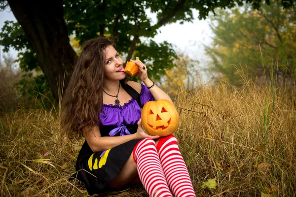 Jeune femme en costume de sorcière Halloween dans la forêt d'automne avec citrouille jaune . — Photo