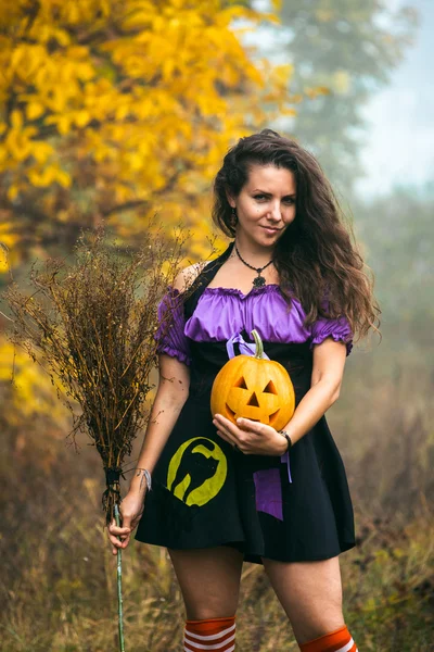 Jeune femme en costume de sorcière Halloween dans la forêt d'automne avec citrouille jaune . — Photo