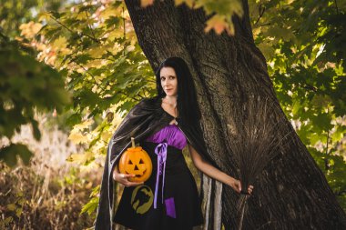 Cadılar Bayramı da genç kadın cadı kostüm sarı kabak ile sonbahar ormandaki.