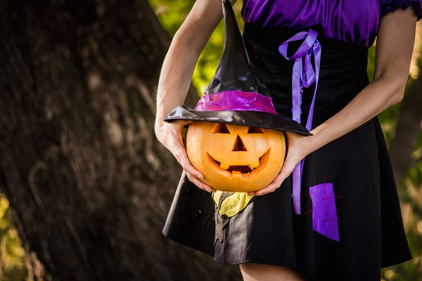 Femme de fantaisie sur Halloween dans la forêt, tenant dans les mains citrouille avec visage sculpté — Photo