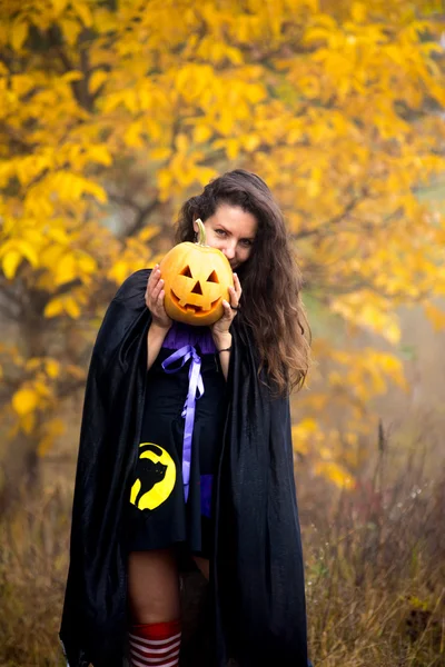 Jeune femme en costume de sorcière Halloween dans la forêt d'automne avec citrouille jaune . — Photo