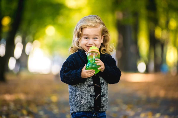 Niña linda bebiendo de la botella afuera en el parque — Foto de Stock