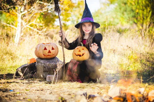 Vrolijke Halloween. Schattige kleine heks met een pompoen in handen van het vuur. — Stockfoto