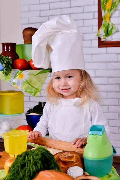 Маленькая девочка в одежде повара крутит кружок теста на столе — стоковое фото